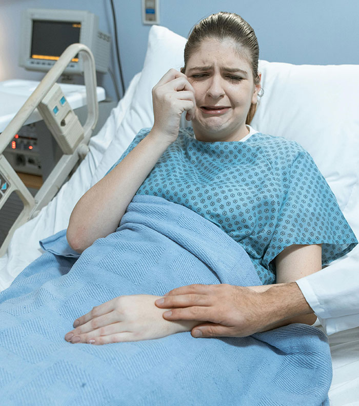 A young woman crying in a hospital bed, a hand comforting her. Reminiscent of messed up school stories.