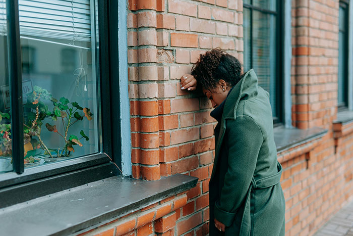 A distraught woman leans against a brick wall, reflecting on messed up school stories and younger years.