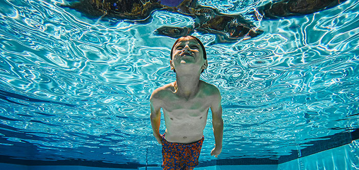 Underwater view of a boy blowing bubbles, looking up at the rippling surface. A good school story image.