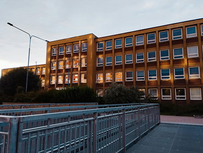 A large school building at sunset, with light reflecting in windows and a metal railing in the foreground, showing school stories.