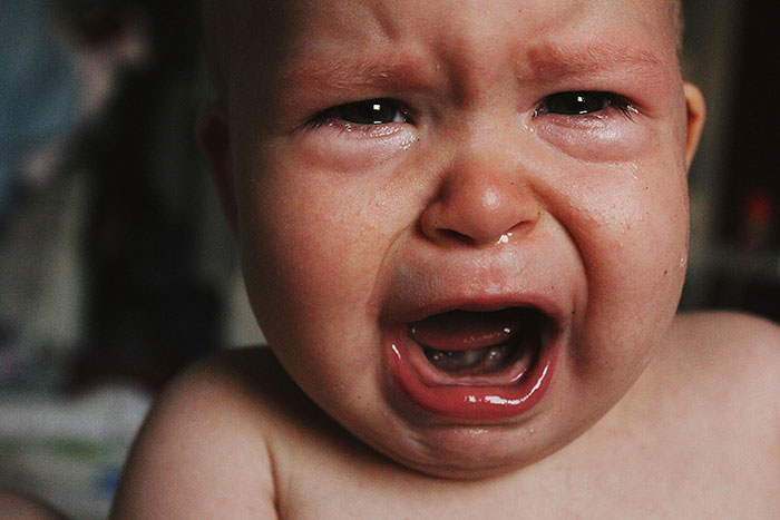 Close-up of a crying baby, tears streaming, mouth open wide in distress. Younger years might not always be easy.