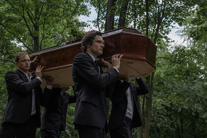Men in black suits carrying a coffin through a forest. This image represents the theme of messed up school stories.