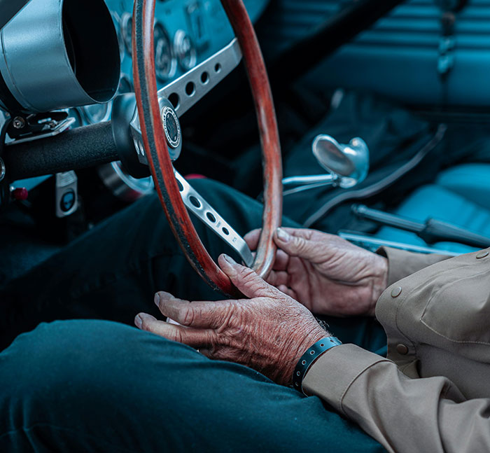 Close-up of weathered hands gripping a vintage car steering wheel, evoking memories of younger years and school stories.