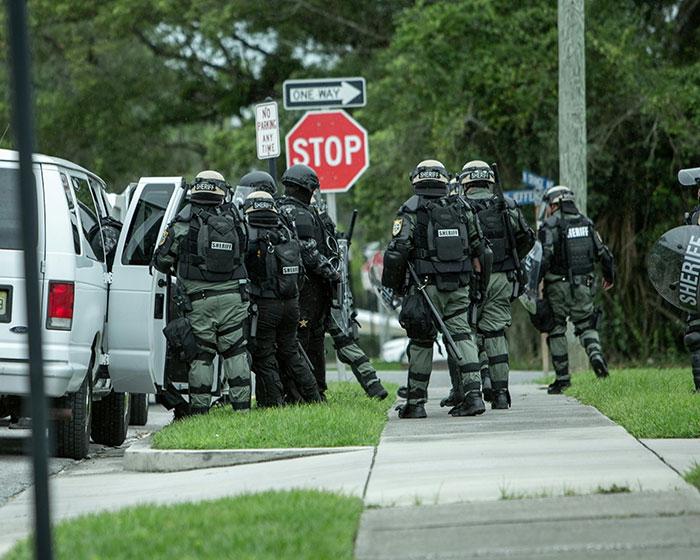 SWAT team officers with riot gear stand by a van. Reflect on messed up school stories and appreciate younger years.