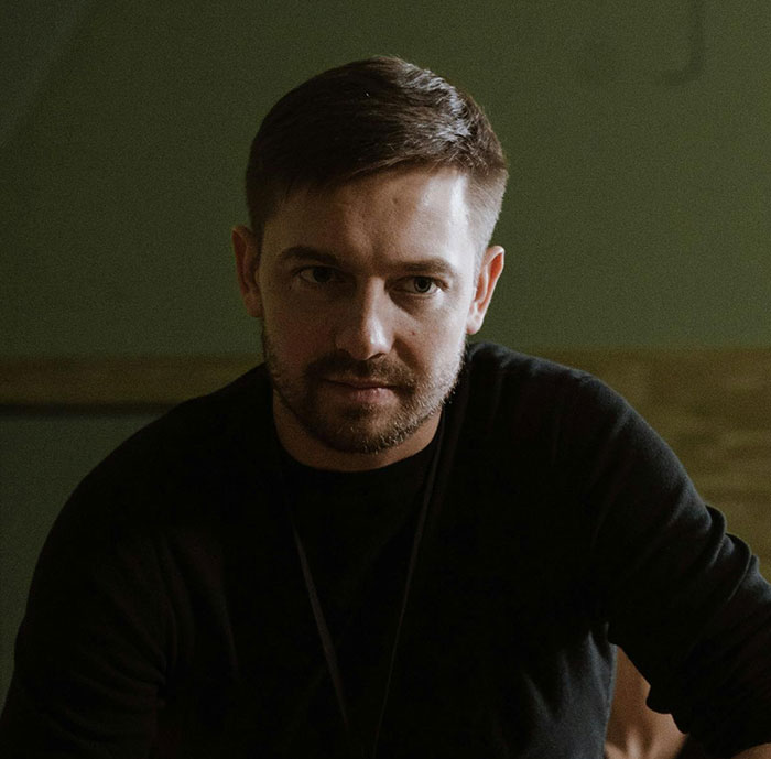 A man with short hair and a beard, wearing a dark shirt, looking intently. Many messed up school stories here.