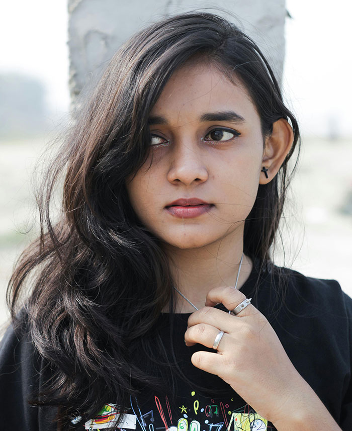 A young woman with long dark hair, wearing a black top and silver rings, looking sideways. School stories keyword.