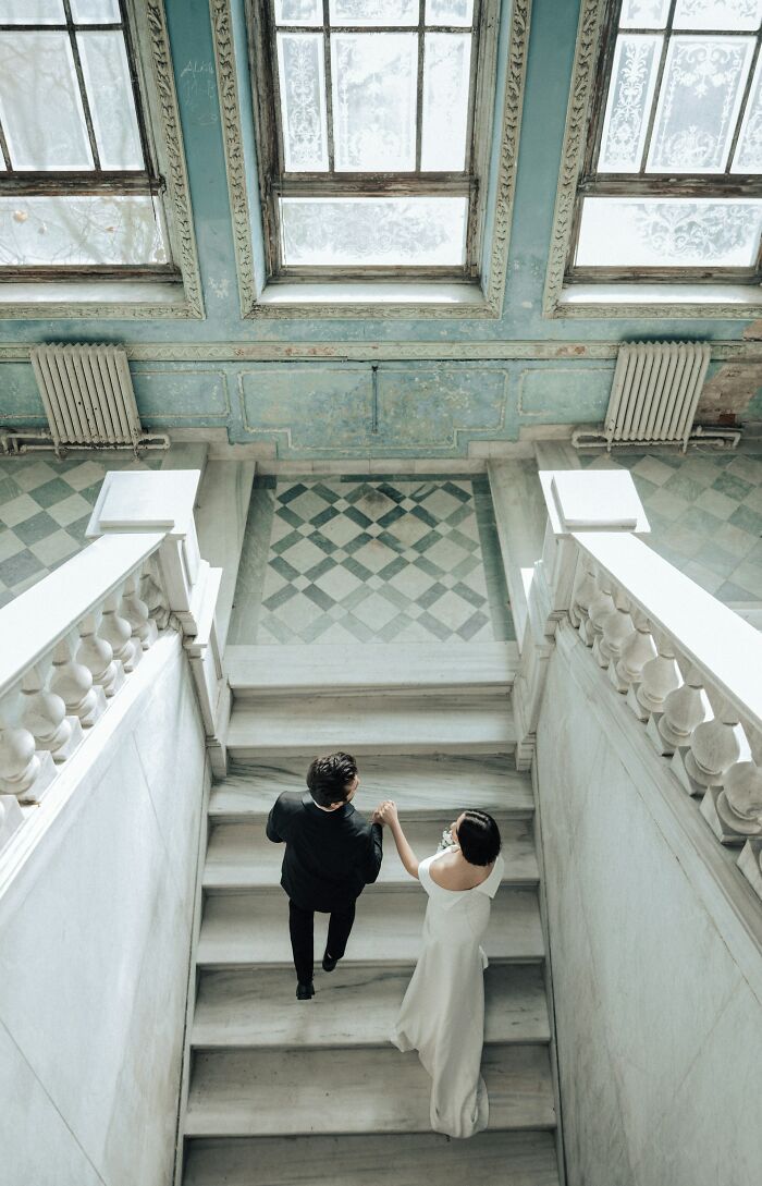 Couple holding hands walking up marble stairs inside historic building in situationship setting