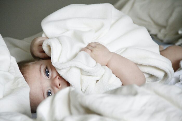 Baby peeking from under a white blanket in bed