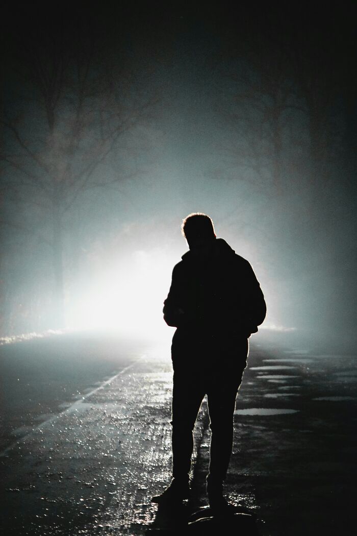 A silhouetted figure stands on a wet road, facing a bright, eerie light in the fog. Very creepy things experienced.
