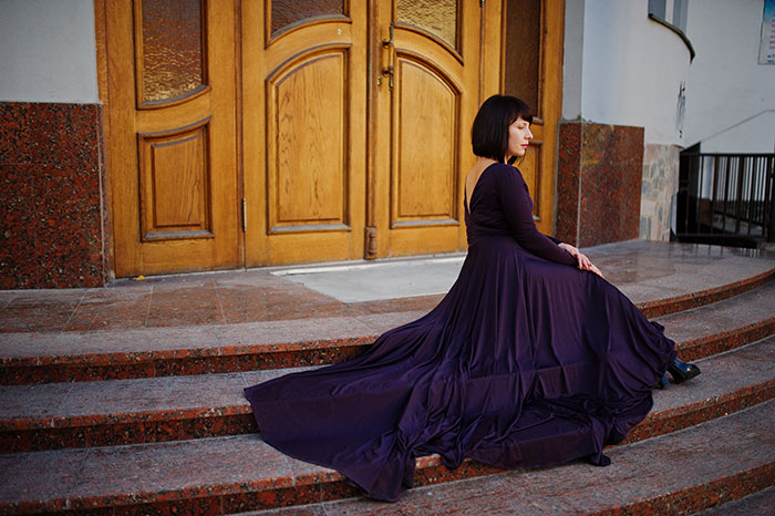 Woman in royal purple gown sitting on steps outside building Woman in royal purple gown sitting on steps outside building