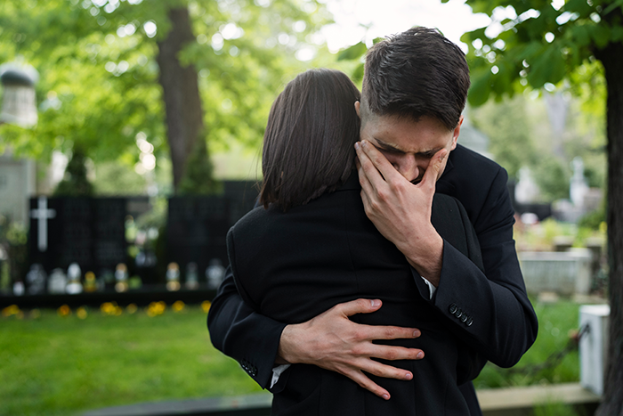 Man in suit crying and hugging woman grieving at cemetery