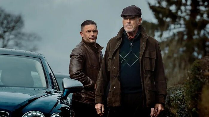 Tom Hardy and co-star standing outside near a car in a scene from Mobland Tom Hardy and co-star standing outside near a car in a scene from Mobland