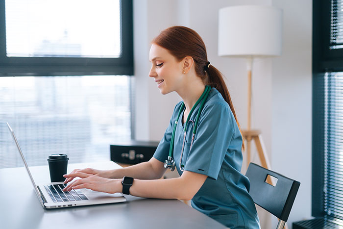 Woman in scrubs working on laptop representing SAHM traditional values