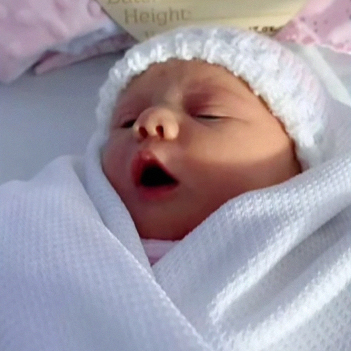 Newborn baby wrapped in white blanket yawning