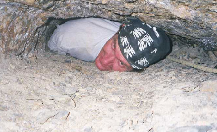 Man squeezing through narrow rocky cave entrance