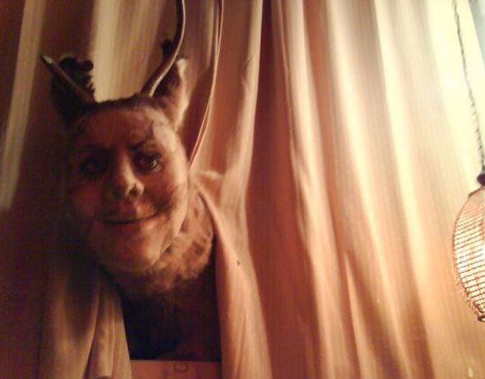 Dark image of a creepy human-like face with horns behind curtain