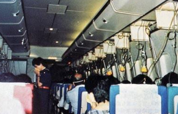Interior of an airplane with passengers seated and a flight attendant standing