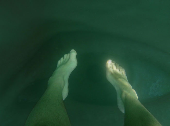 Person's legs submerged underwater with green murky surroundings