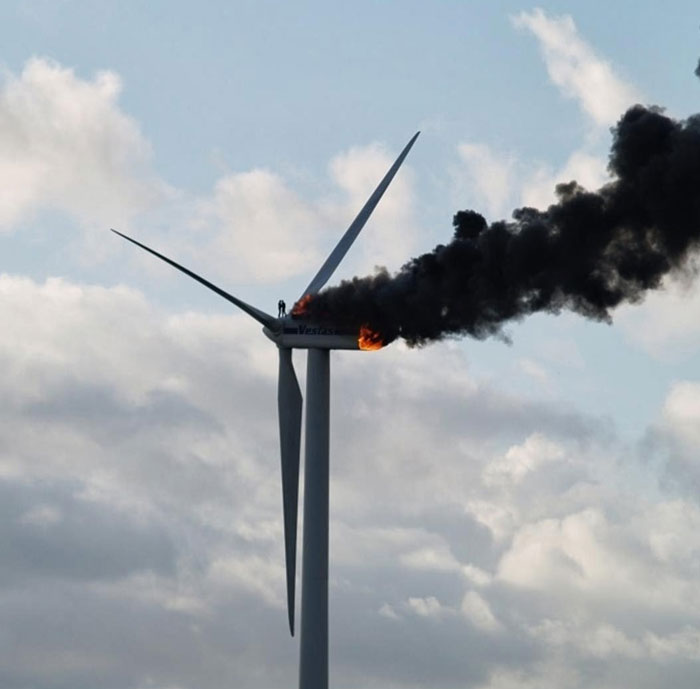 Wind turbine on fire with thick black smoke at top