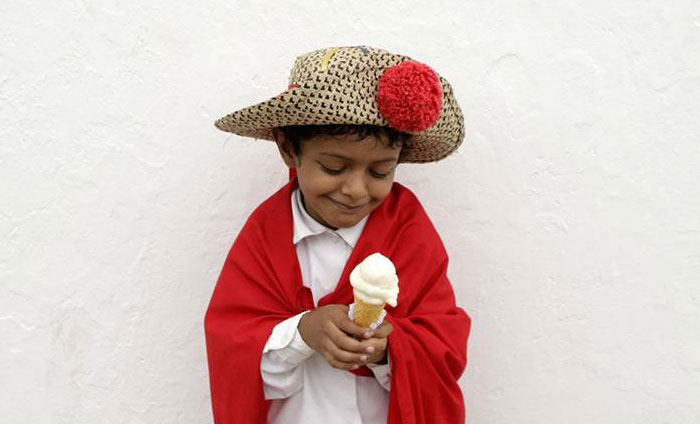 Powerful photo of a smiling boy in traditional clothing holding an ice cream cone