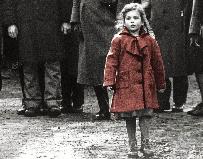 Powerful photo of a young girl in a red coat standing among adults