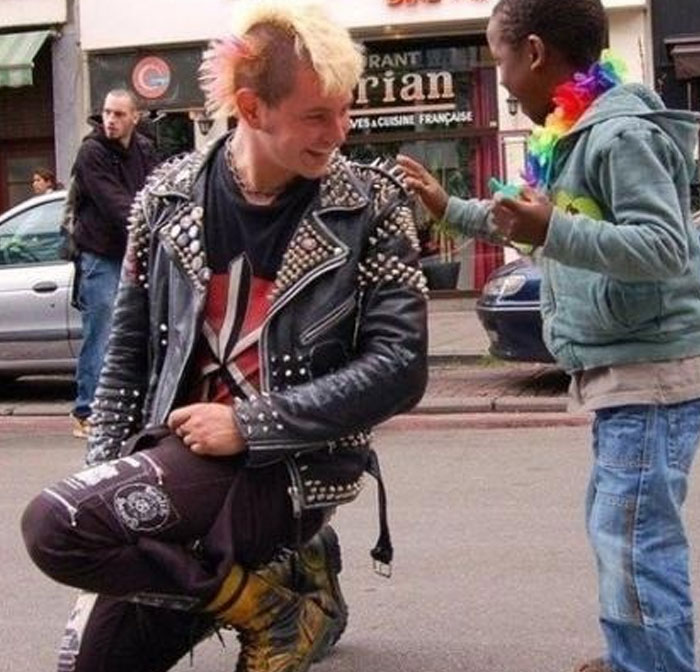 Punk teenager with dyed hair smiling and interacting with child on street