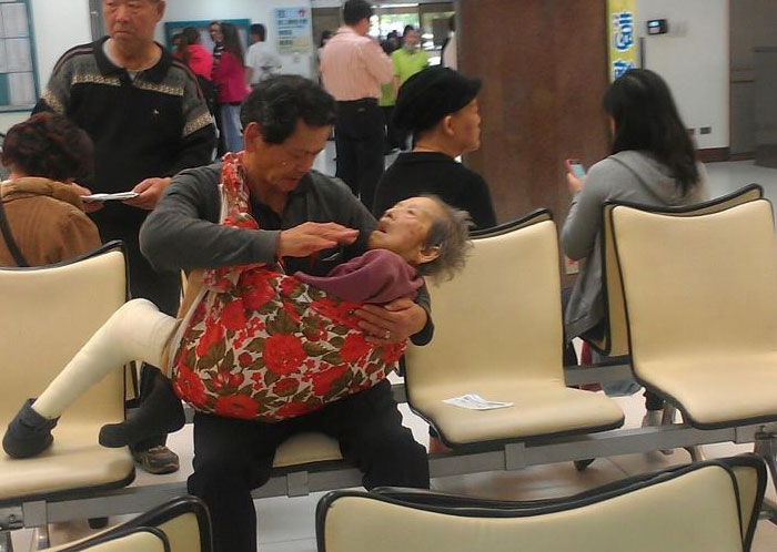 Powerful photo of man carrying elderly woman in crowded public waiting area