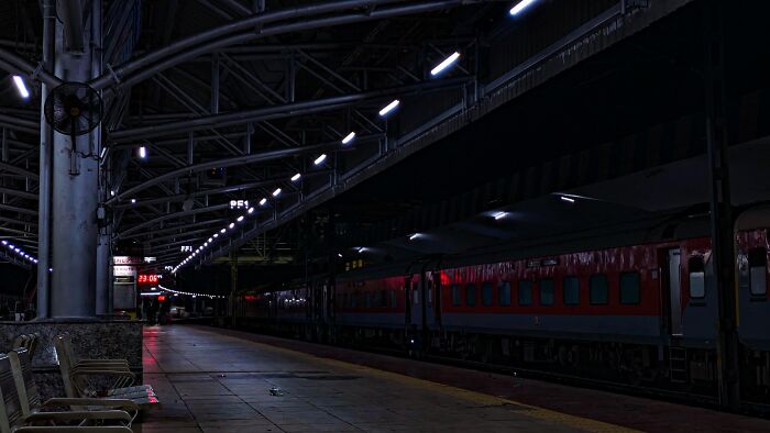 Dark train station platform illuminated by lights with empty benches in random camera click