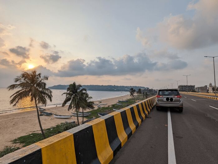 Sunset view of beach and road with car parked beside palm trees in random camera click