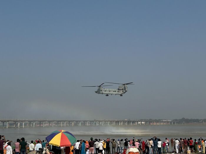 Crowd watching helicopter flying over river creating mist in incredible random photo
