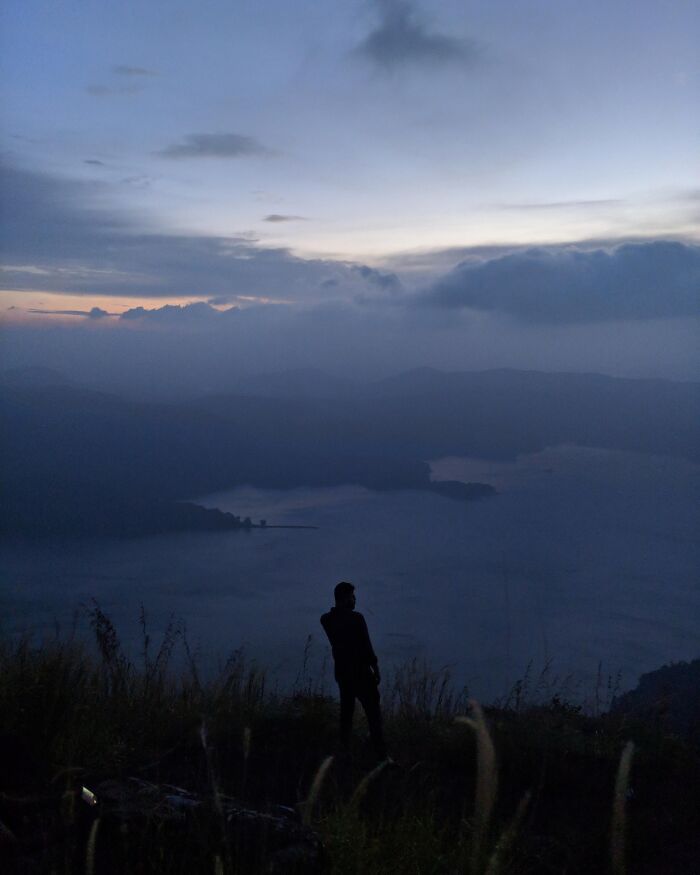 Person standing on hill overlooking misty lake and mountains during random camera click