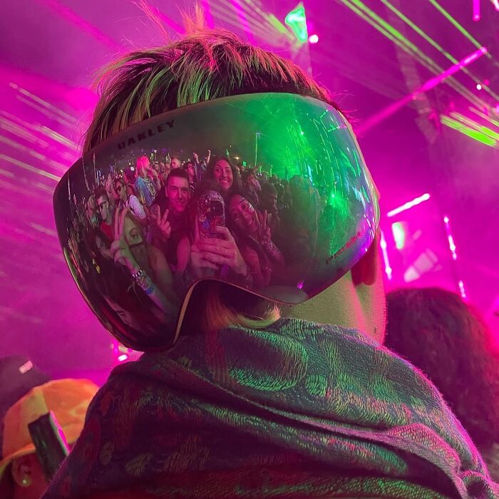 Concert crowd reflected in large reflective goggles during colorful light show