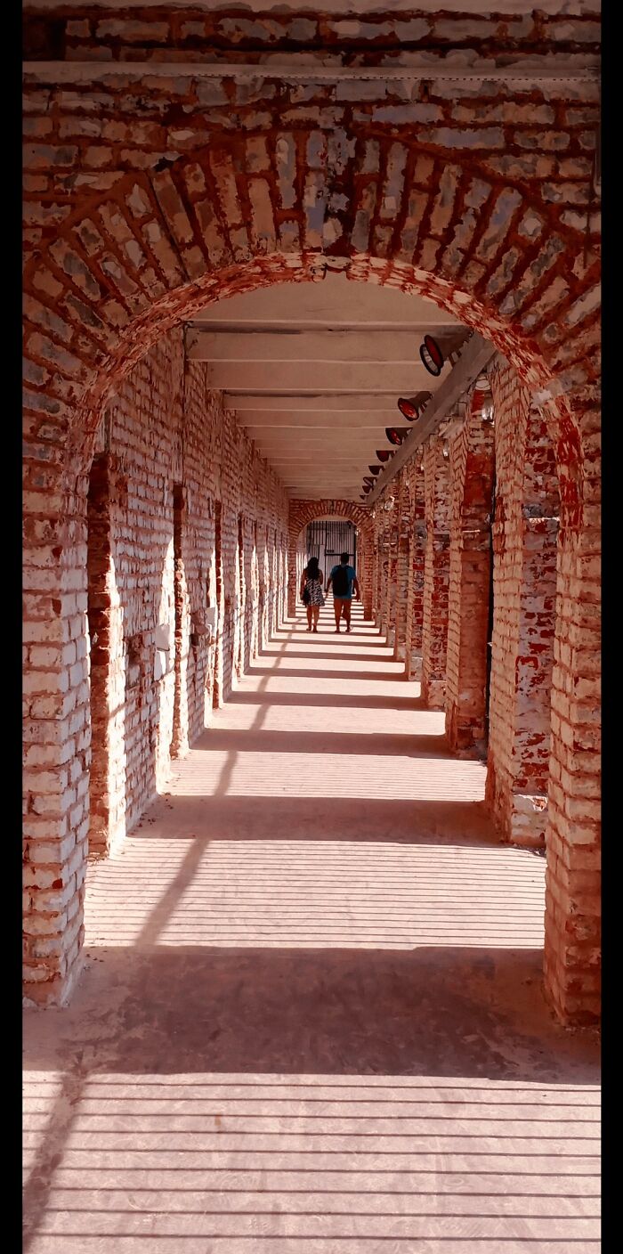 Sunlit arched brick corridor with couple walking, showcasing incredible architecture photos