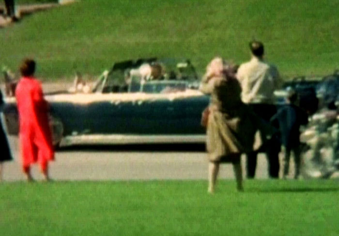 Vintage photo of people watching a motorcade with a convertible car driving on a road