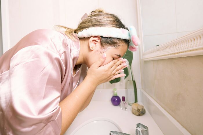 Woman washing face absentmindedly in bathroom depicting brain on auto pilot action