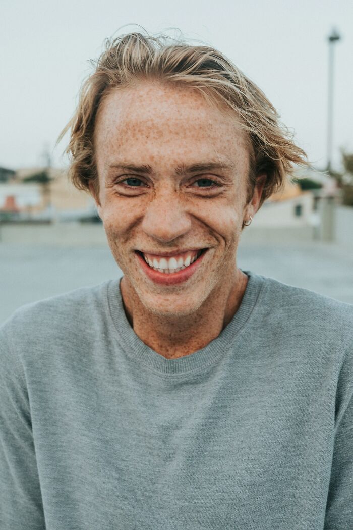 Smiling freckled young man in casual grey sweater outdoors