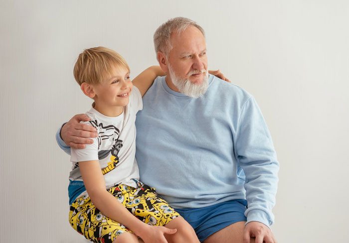 Grandfather hugging smiling young boy sitting on his lap in casual clothes