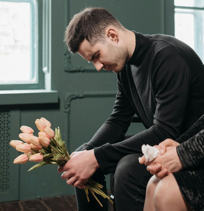 Young man grieving and holding flowers indoors