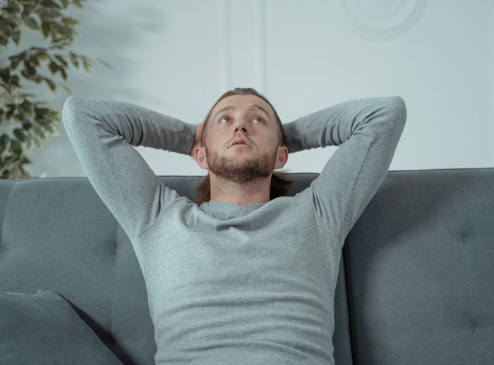 Man in gray shirt looking up, appearing thoughtful on couch, reflecting on toxic parents story