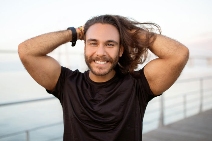 Smiling man with long hair, hands behind his head, in a black shirt, embodying a funny running neighbor. Smiling man with long hair, hands behind his head, in a black shirt, embodying a funny running neighbor.