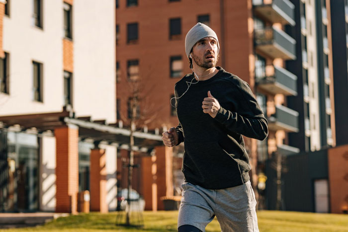 A man running with headphones and a beanie in an urban setting, illustrating the neighbor running story. A man running with headphones and a beanie in an urban setting, illustrating the neighbor running story.