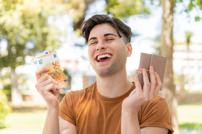 Young man happily holding cash and wallet outdoors