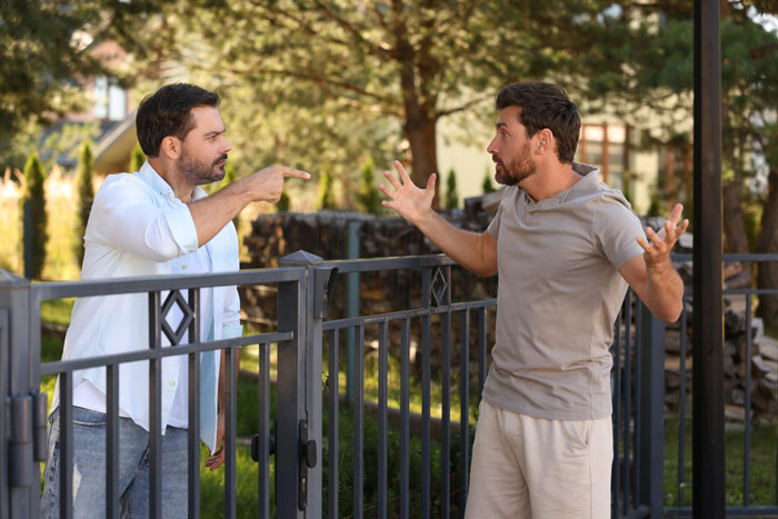 Two men arguing angrily over a damaged neighbor's fence conflict