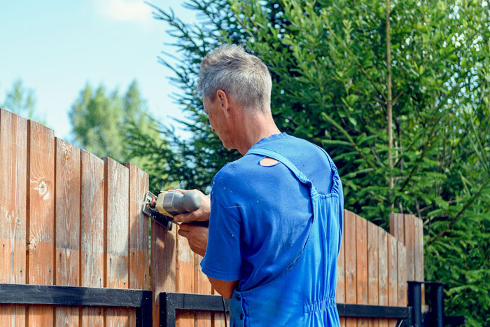 Man repairing wooden fence with electric sander