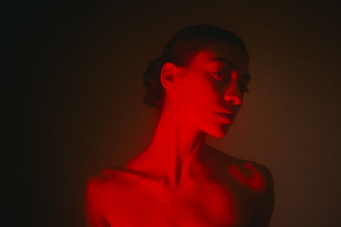 A young woman's face and upper body are bathed in intense red light, highlighting scientific facts like how crows hold a grudge.