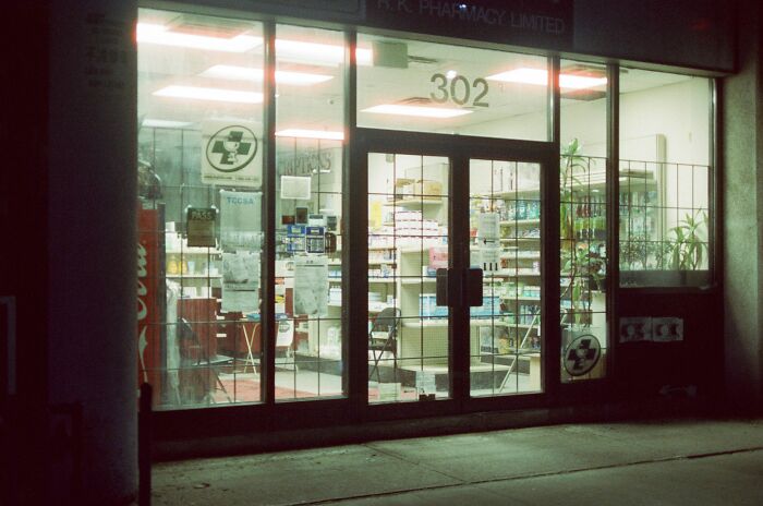 Pharmacy storefront illuminated at night showing medicine shelves inside
