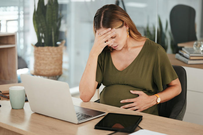 Pregnant woman stressed while working at a desk with laptop and tablet Pregnant woman stressed while working at a desk with laptop and tablet