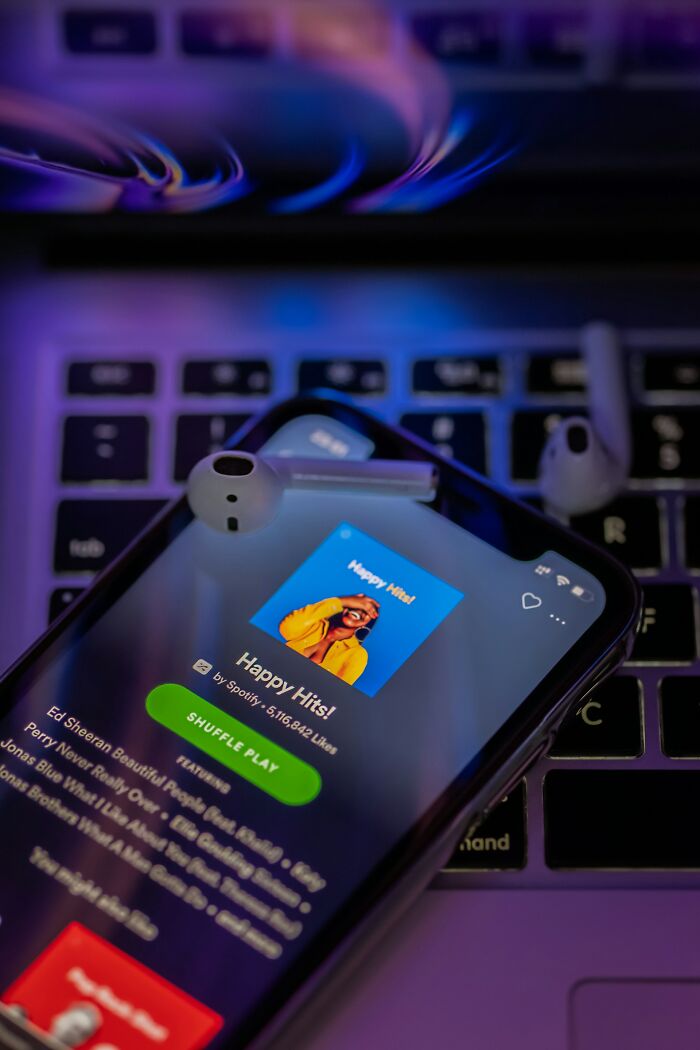A smartphone displaying the Spotify "Happy Hits!" playlist, with earbuds resting on it. A smart scale offers similar revelations.