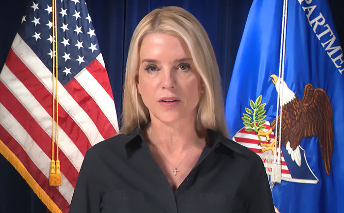 Former Attorney General Pam Bondi speaking at a podium with US and Department of Justice flags