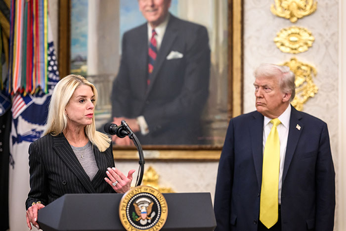 Pam Bondi speaking at a presidential podium with Donald Trump listening nearby